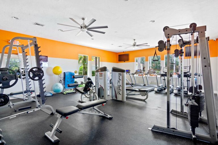 Fitness center with modern weight equiptment, treadmills, two large ceiling fans and two tvs on the wall.