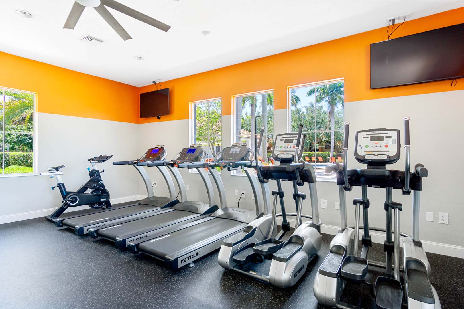 Fitness center with treadmills, ellipticals and excercise bike with large ceiling fan and two tvs on the wall.