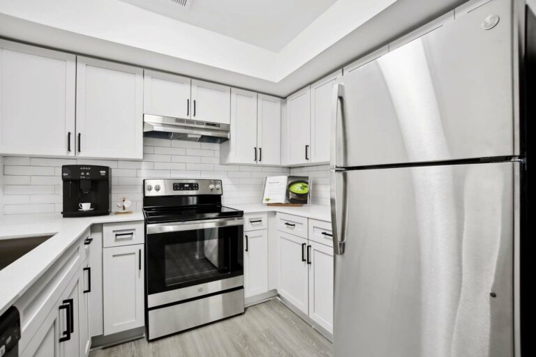 Kitchen with hardwood-style flooring, white quartz counter tops, white subway style backsplash, white shaker cabinets, stainless steel glass top stove and stainless-steel refrigerator.
