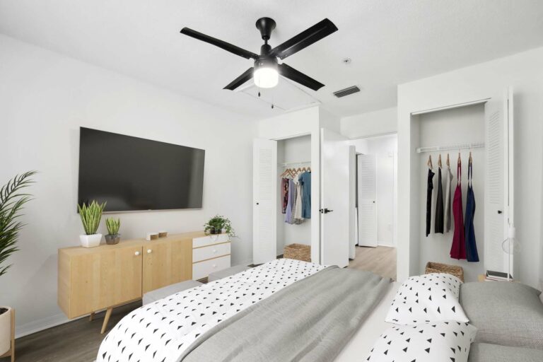 Virtually staged bedroom with a bed, dresser, nightstand, hardwood-style flooring, ceiling fan, and reach in closets on either side of door